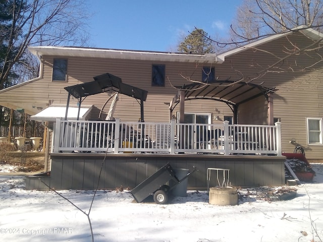 snow covered rear of property with a wooden deck and a pergola