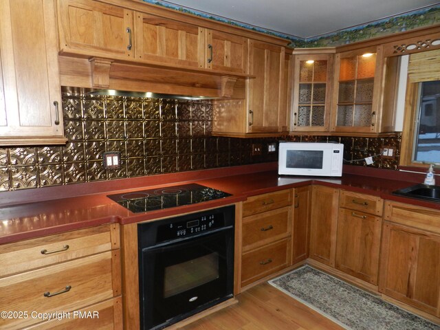 kitchen featuring premium range hood, sink, light hardwood / wood-style flooring, and black appliances