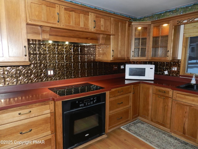 kitchen featuring dark countertops, light wood-style flooring, glass insert cabinets, ventilation hood, and black appliances