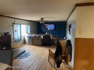 living room featuring crown molding, ceiling fan, wooden walls, and light wood-type flooring