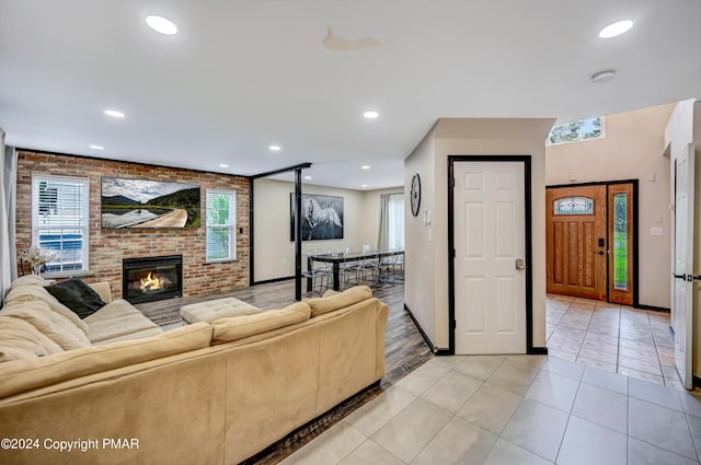 living room featuring light tile patterned floors, recessed lighting, brick wall, a fireplace, and baseboards