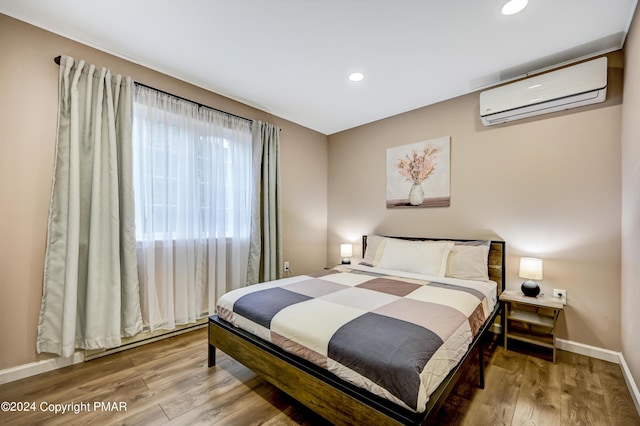 bedroom with a wall mounted AC, recessed lighting, wood finished floors, and baseboards