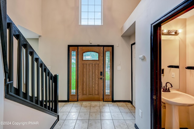 foyer entrance with a towering ceiling, light tile patterned floors, plenty of natural light, and stairway