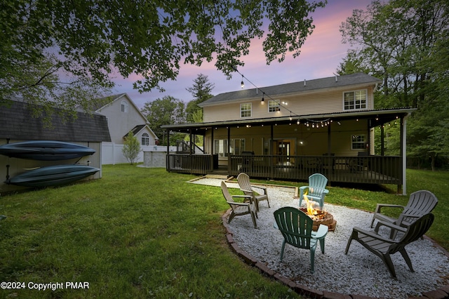 back of property at dusk with a fire pit, a yard, a deck, and fence