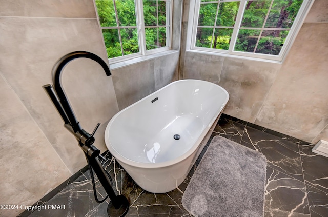 bathroom with a freestanding bath, marble finish floor, and stone wall