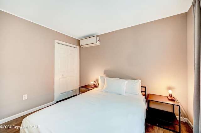 bedroom with a closet, a wall unit AC, baseboards, and wood finished floors