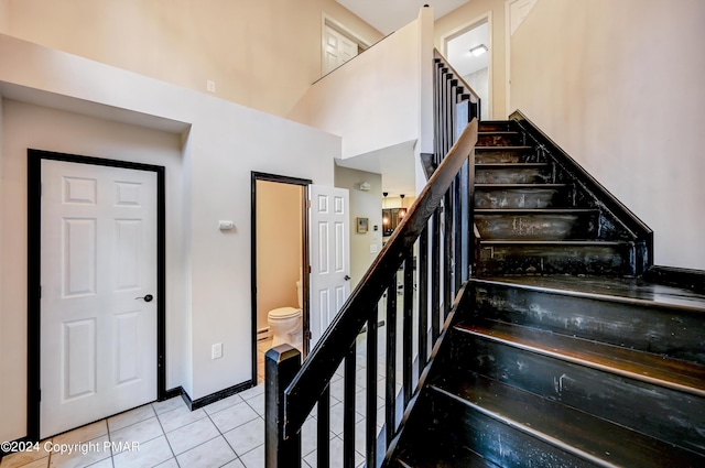 staircase featuring a towering ceiling, tile patterned flooring, and baseboards