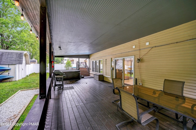 wooden deck featuring an outbuilding, fence, a hot tub, and a storage unit