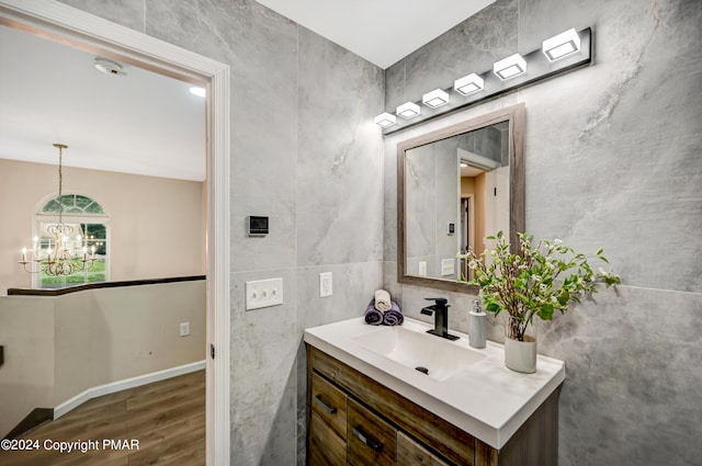 bathroom featuring a chandelier, wood finished floors, vanity, baseboards, and tile walls