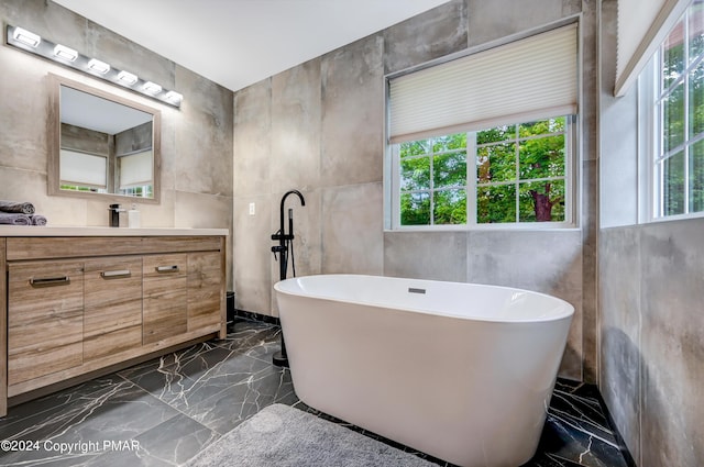 full bathroom featuring marble finish floor, stone wall, a freestanding tub, and vanity