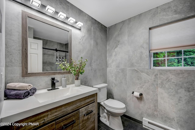 bathroom with toilet, a shower with shower door, vanity, a baseboard heating unit, and tile walls