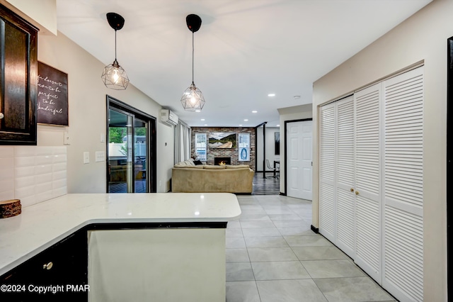 kitchen featuring decorative light fixtures, light countertops, an AC wall unit, a fireplace, and light tile patterned flooring