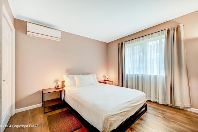 bedroom featuring baseboards, a wall mounted AC, and light wood-style floors