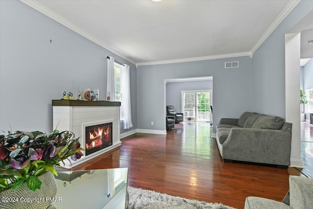 living area with wood finished floors, baseboards, visible vents, ornamental molding, and a glass covered fireplace