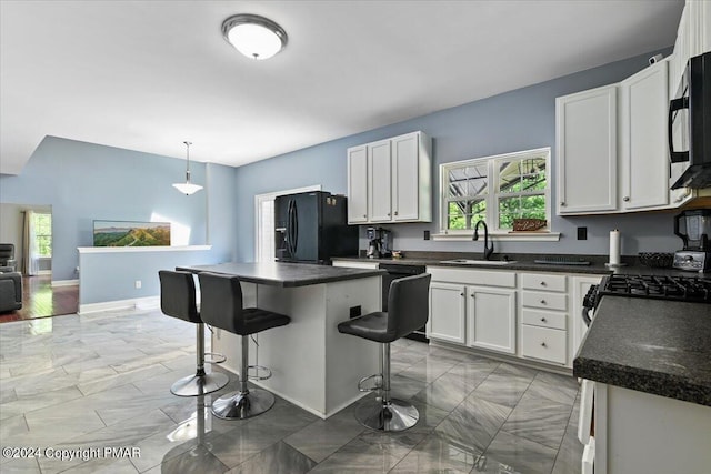 kitchen with a healthy amount of sunlight, black appliances, a kitchen island, white cabinetry, and a sink