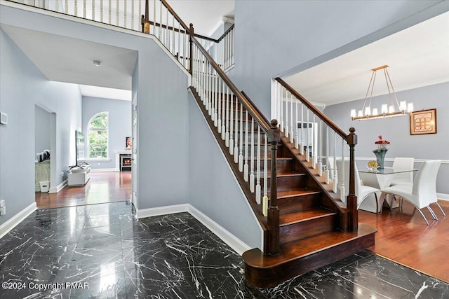 stairs with crown molding, baseboards, a chandelier, a high ceiling, and marble finish floor