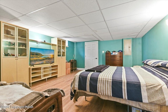 bedroom with baseboards, light wood-type flooring, and a drop ceiling