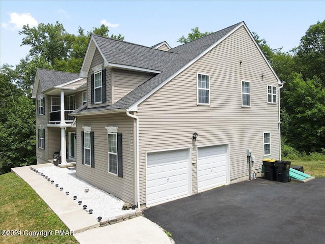 view of side of property with driveway, a garage, and roof with shingles