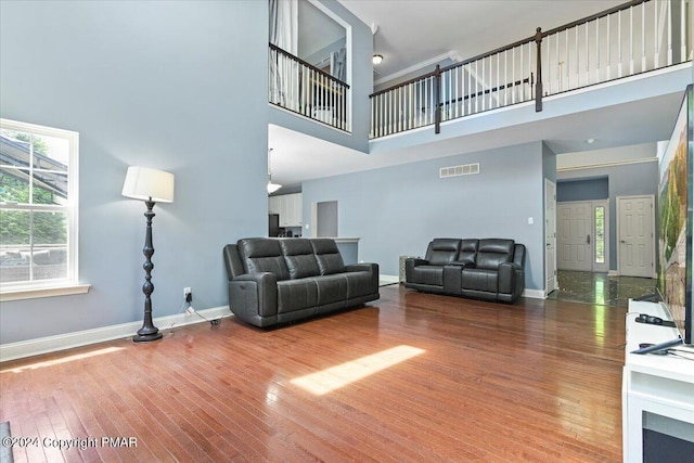 living area with visible vents, baseboards, hardwood / wood-style floors, and a towering ceiling