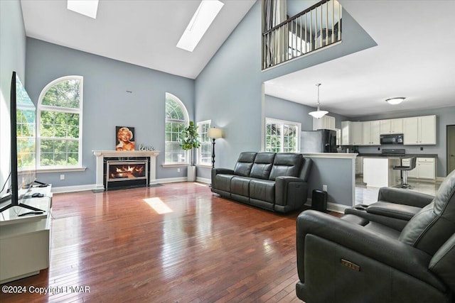 living area with high vaulted ceiling, a fireplace with flush hearth, a skylight, and hardwood / wood-style flooring