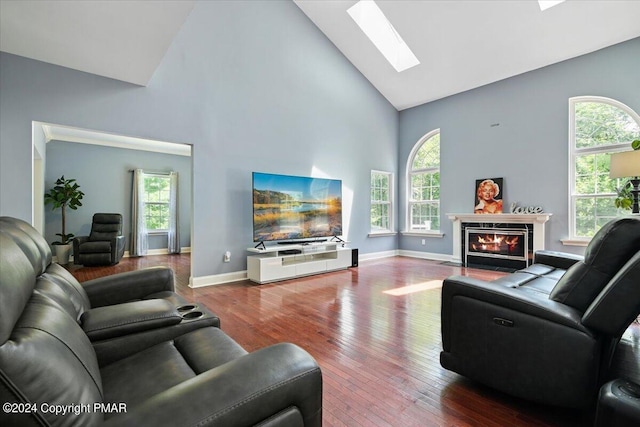 living area featuring baseboards, a fireplace with flush hearth, a skylight, hardwood / wood-style flooring, and high vaulted ceiling