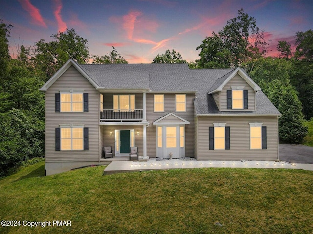 rear view of house featuring a lawn, a patio, a shingled roof, and a balcony