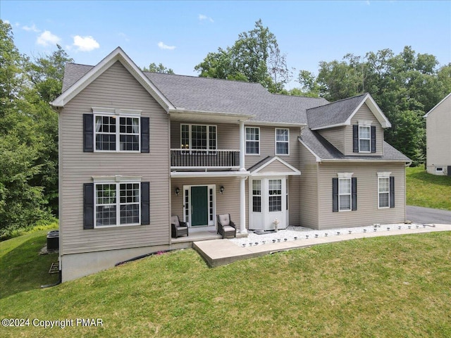 view of front facade with a patio, a front lawn, a balcony, and roof with shingles