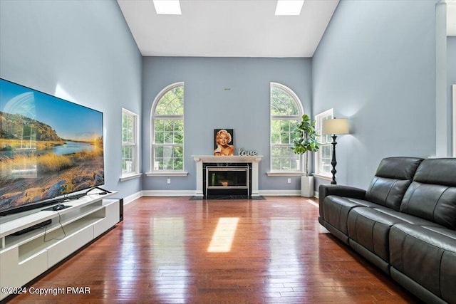 living room featuring a fireplace, high vaulted ceiling, baseboards, and hardwood / wood-style flooring