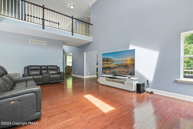 living room with visible vents, baseboards, hardwood / wood-style floors, and a towering ceiling