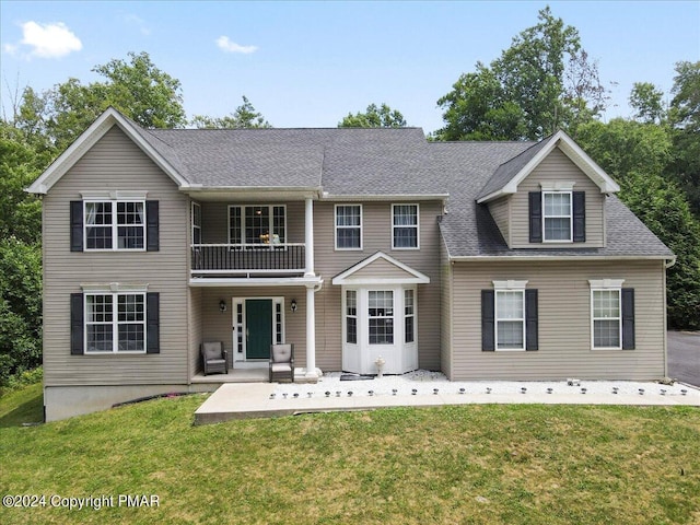 view of front of property featuring a front lawn, a balcony, roof with shingles, and a patio