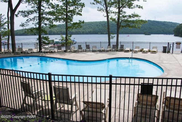 pool with a patio area, fence, and a water view