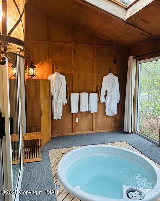 bathroom with lofted ceiling with skylight, wooden walls, and a garden tub