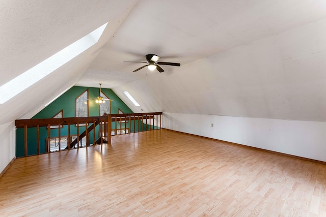 additional living space with lofted ceiling with skylight, wood finished floors, a ceiling fan, and baseboards