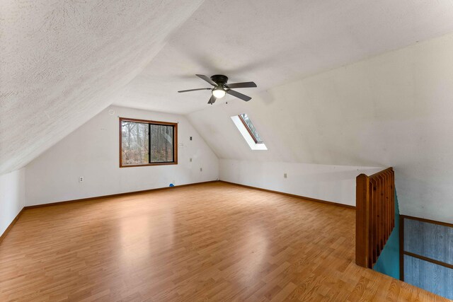 additional living space featuring lofted ceiling with skylight, baseboards, a textured ceiling, and wood finished floors