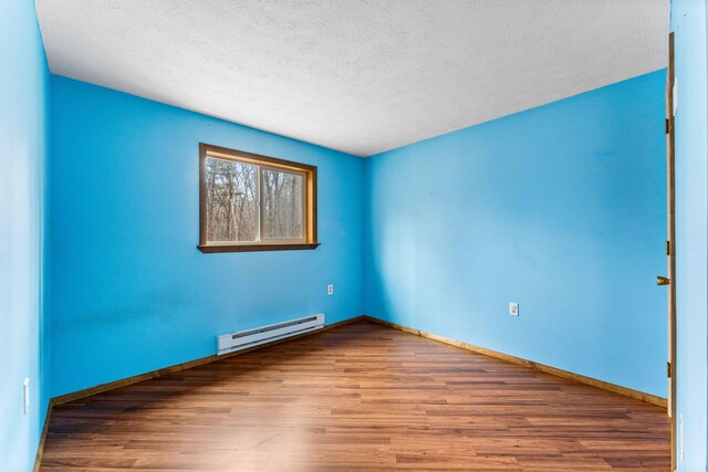 empty room with a textured ceiling, baseboards, baseboard heating, and wood finished floors