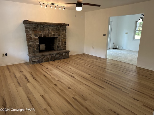 unfurnished living room featuring baseboards, a ceiling fan, wood finished floors, and a stone fireplace