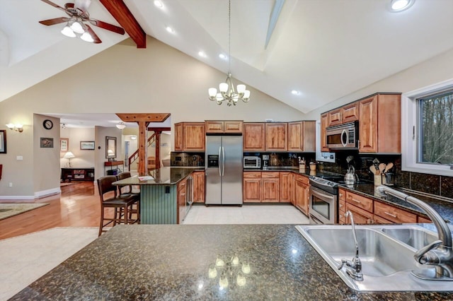 kitchen with a sink, appliances with stainless steel finishes, a kitchen bar, beamed ceiling, and brown cabinets