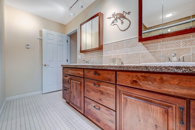 full bathroom with track lighting, backsplash, baseboards, double vanity, and a sink