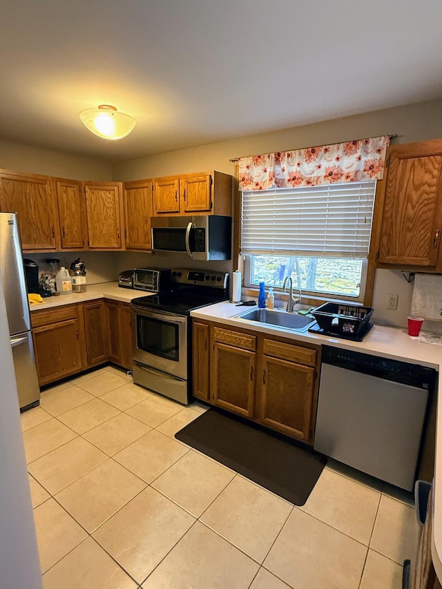 kitchen featuring brown cabinets, light tile patterned floors, stainless steel appliances, and a sink