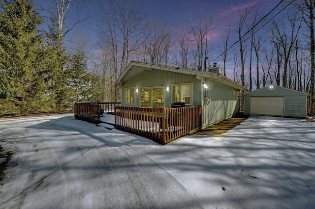 view of front of property with an outbuilding, a detached garage, a chimney, driveway, and a wooden deck