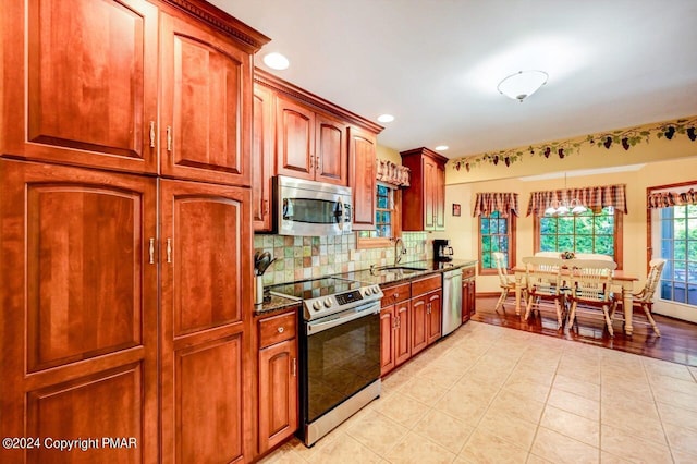 kitchen featuring light tile patterned floors, decorative backsplash, dark stone countertops, stainless steel appliances, and a sink