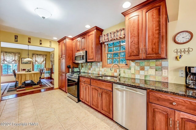 kitchen with stainless steel appliances, a sink, dark stone countertops, and tasteful backsplash