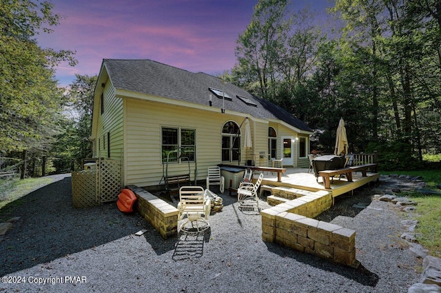 back of house at dusk with entry steps, roof with shingles, and a wooden deck