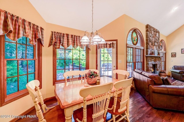 dining area with dark wood-type flooring, lofted ceiling, a stone fireplace, and an inviting chandelier