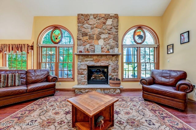 living area featuring a healthy amount of sunlight, vaulted ceiling, a stone fireplace, and wood finished floors