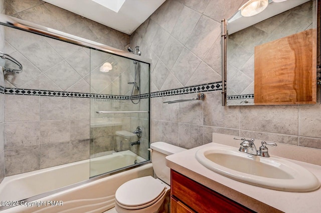 bathroom featuring tile walls, bath / shower combo with glass door, tasteful backsplash, toilet, and vanity