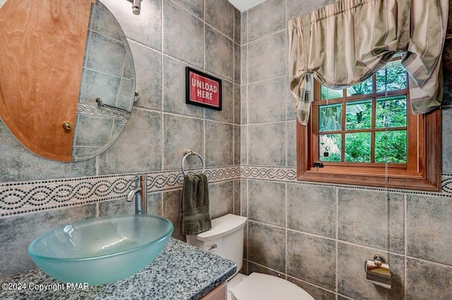 bathroom with toilet, vanity, and tile walls