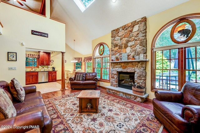 living room with high vaulted ceiling, a skylight, a fireplace, wood finished floors, and decorative columns