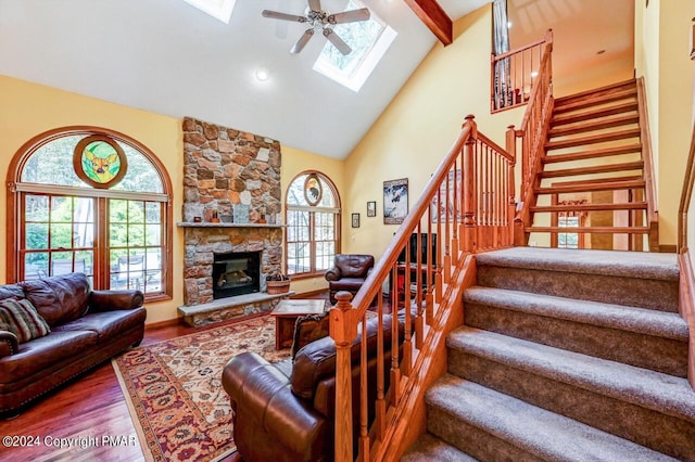 living room featuring a skylight, wood finished floors, stairs, a fireplace, and high vaulted ceiling