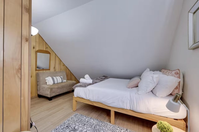 bedroom featuring light wood-style flooring, lofted ceiling, and wooden walls